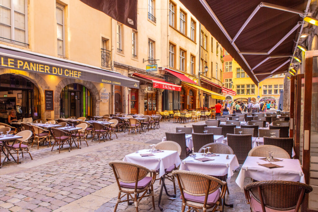 Cozy restaurant seatting in the old quarter of Lyon, France, bustling with diners at twilight.