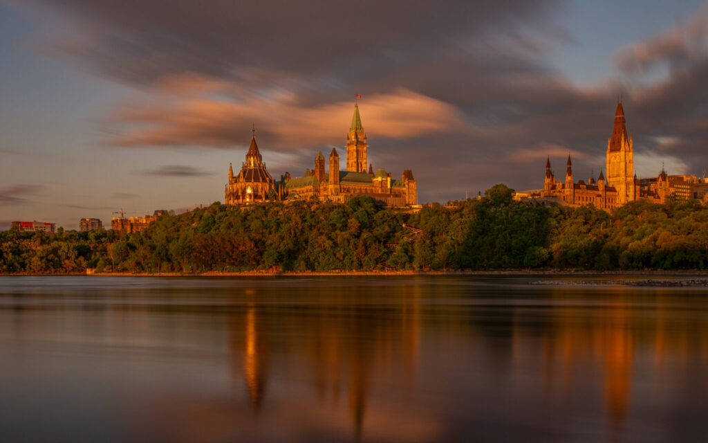 Canadian Parliament illuminated by the warm glow of a beautiful sunset, with vibrant skies casting a stunning backdrop over Ottawa's iconic landmark.