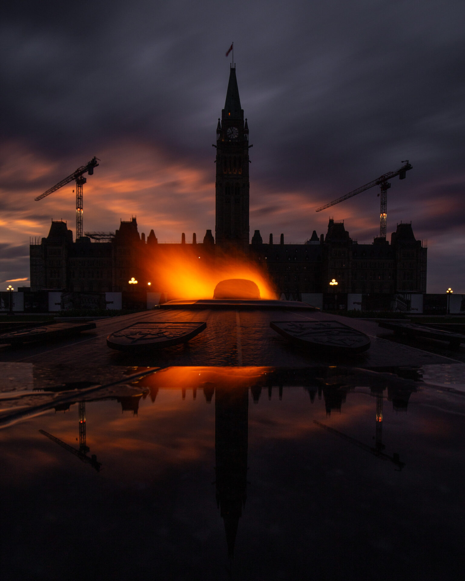 Parliament Hill in Ottawa with a stunning sunset reflecting on the Centennial Flame.