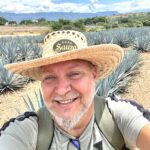 Person wearing a Suaza hat standing in a field of agave plants during a Sauza Tequila tour as I'm Exploring Tequila, Mexico